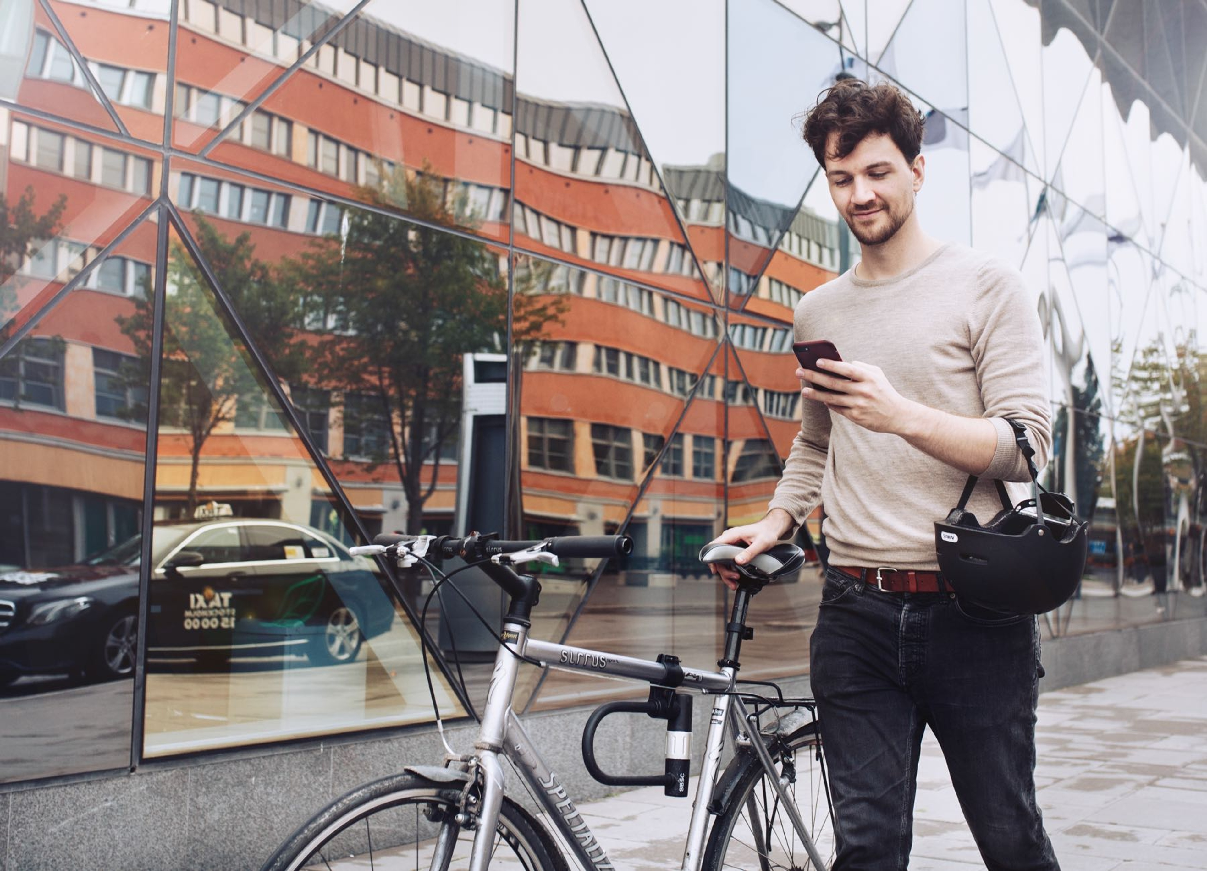 A man holding and looking at his phone while dragging his bike with the other hand