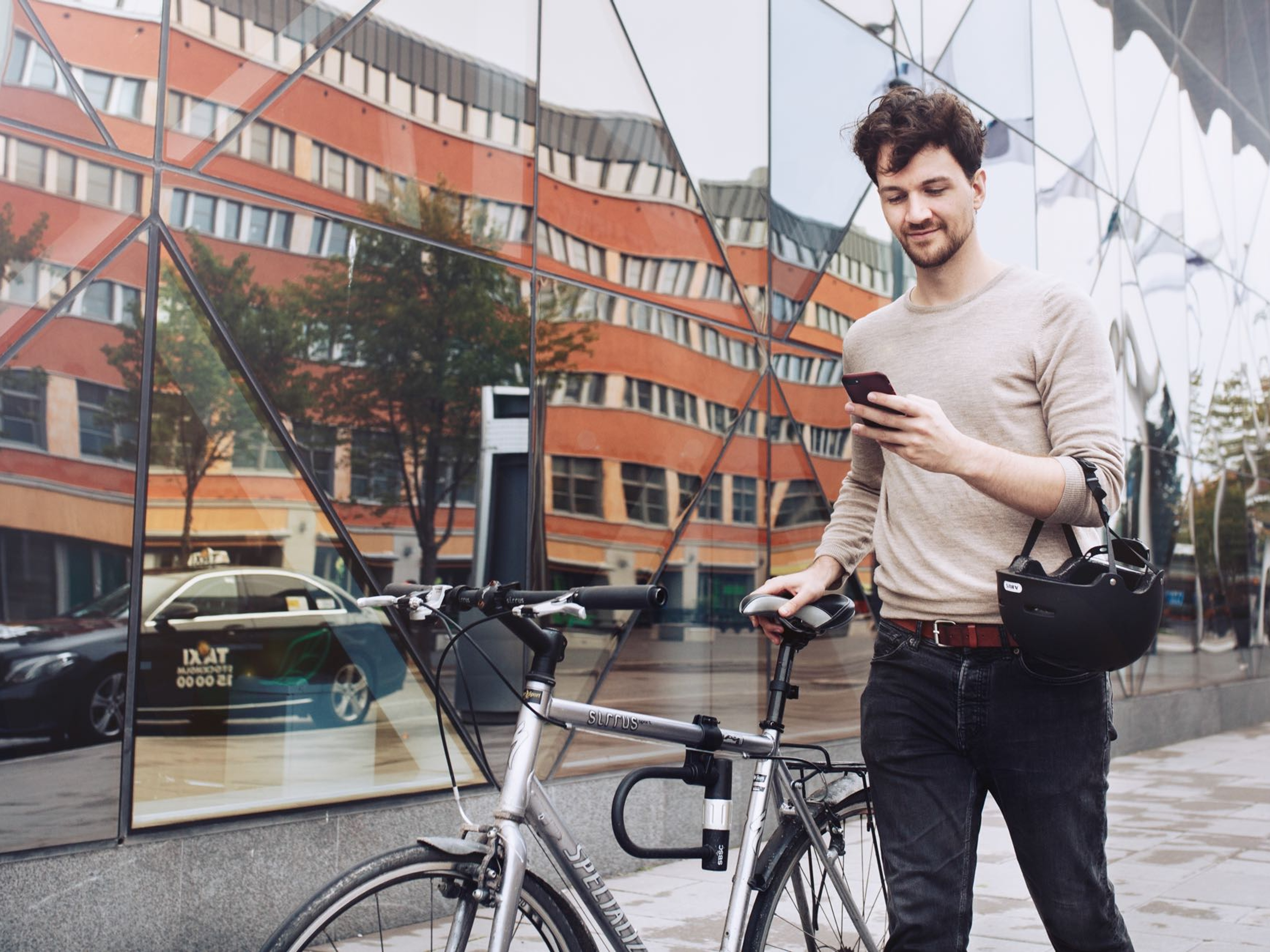 A man holding and looking at his phone while dragging his bike with the other hand