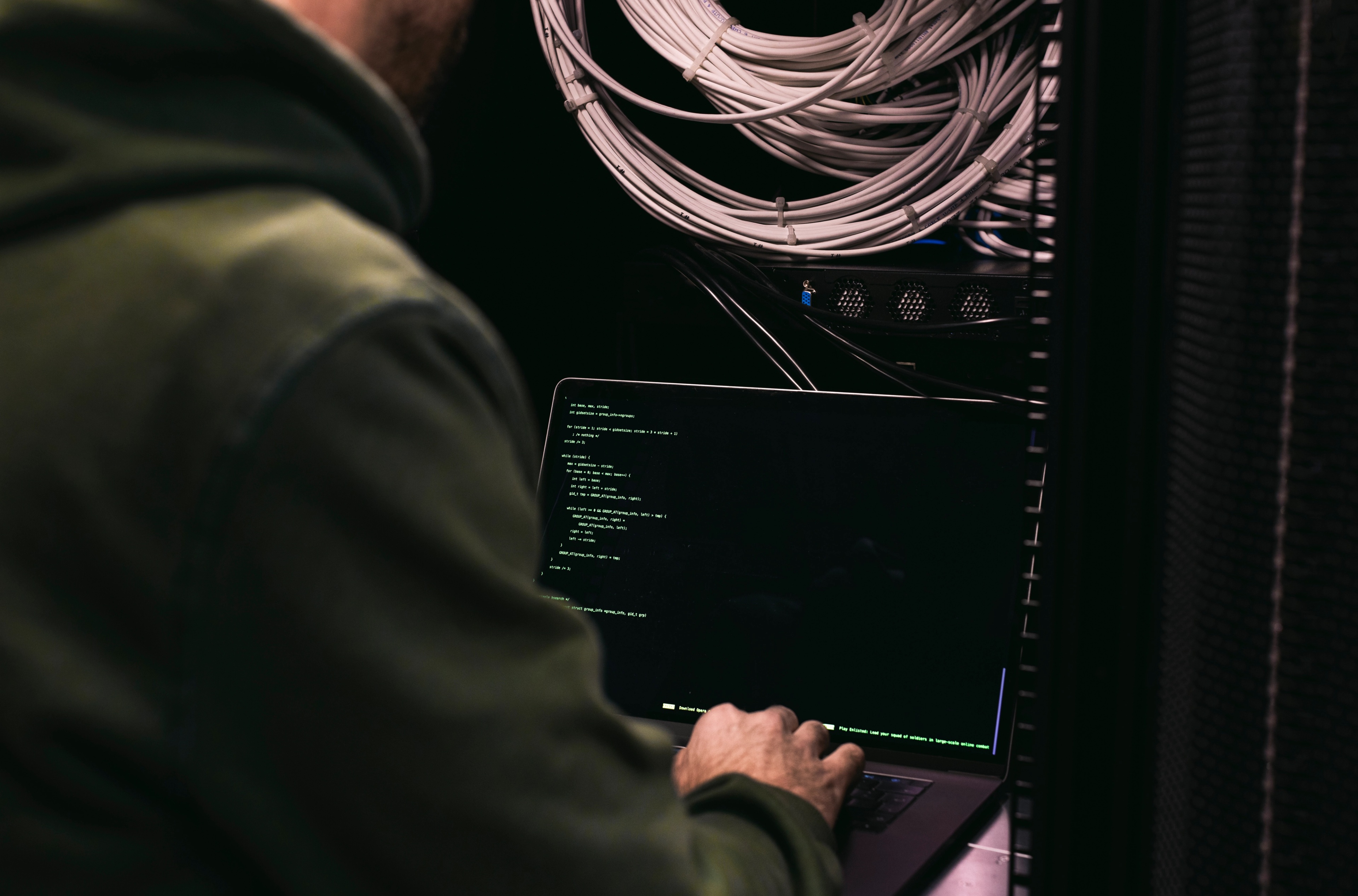 Um homem sentado em frente a um computador em uma sala de servidores.