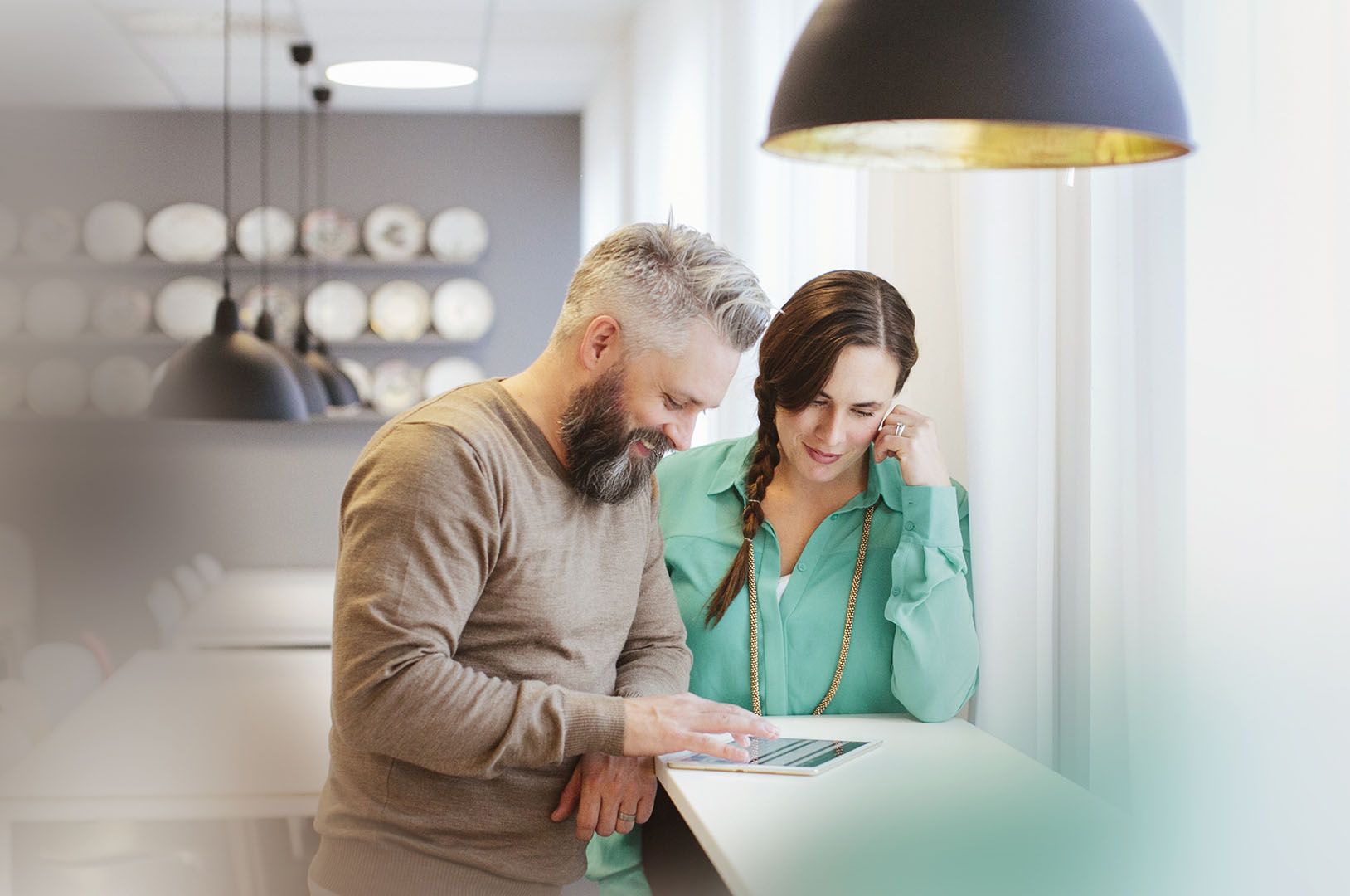 A man and a woman standing at a table looking at a tablet
