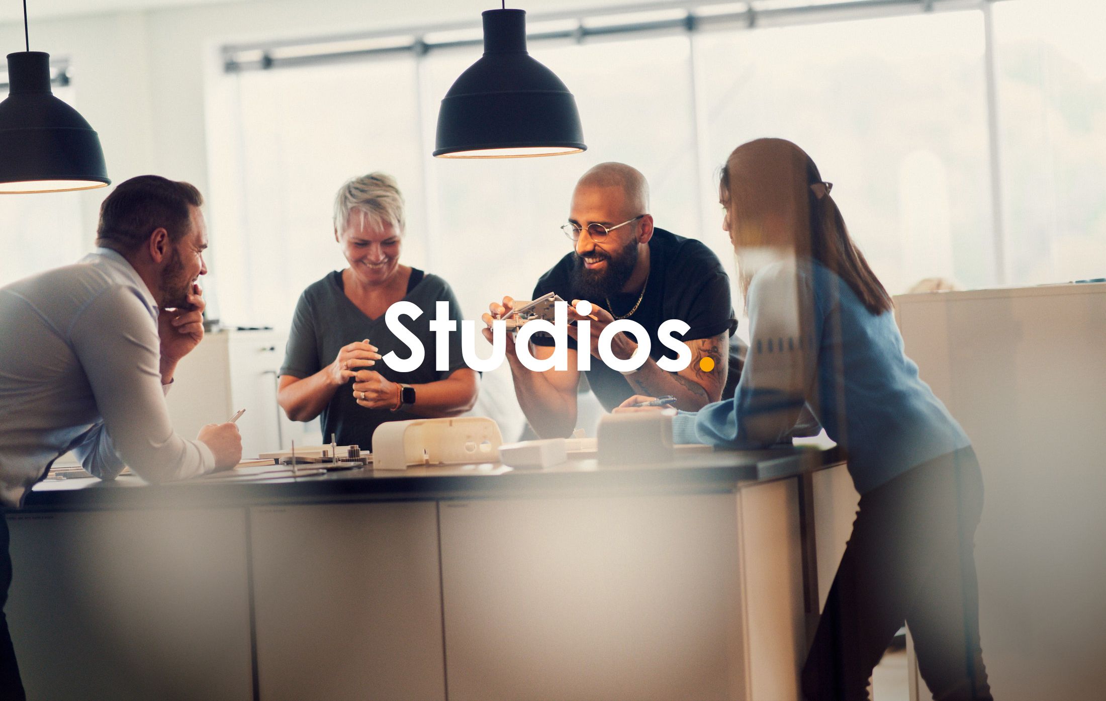 A group of people collaborating around a table with prototypes, and the text studios written across the picture