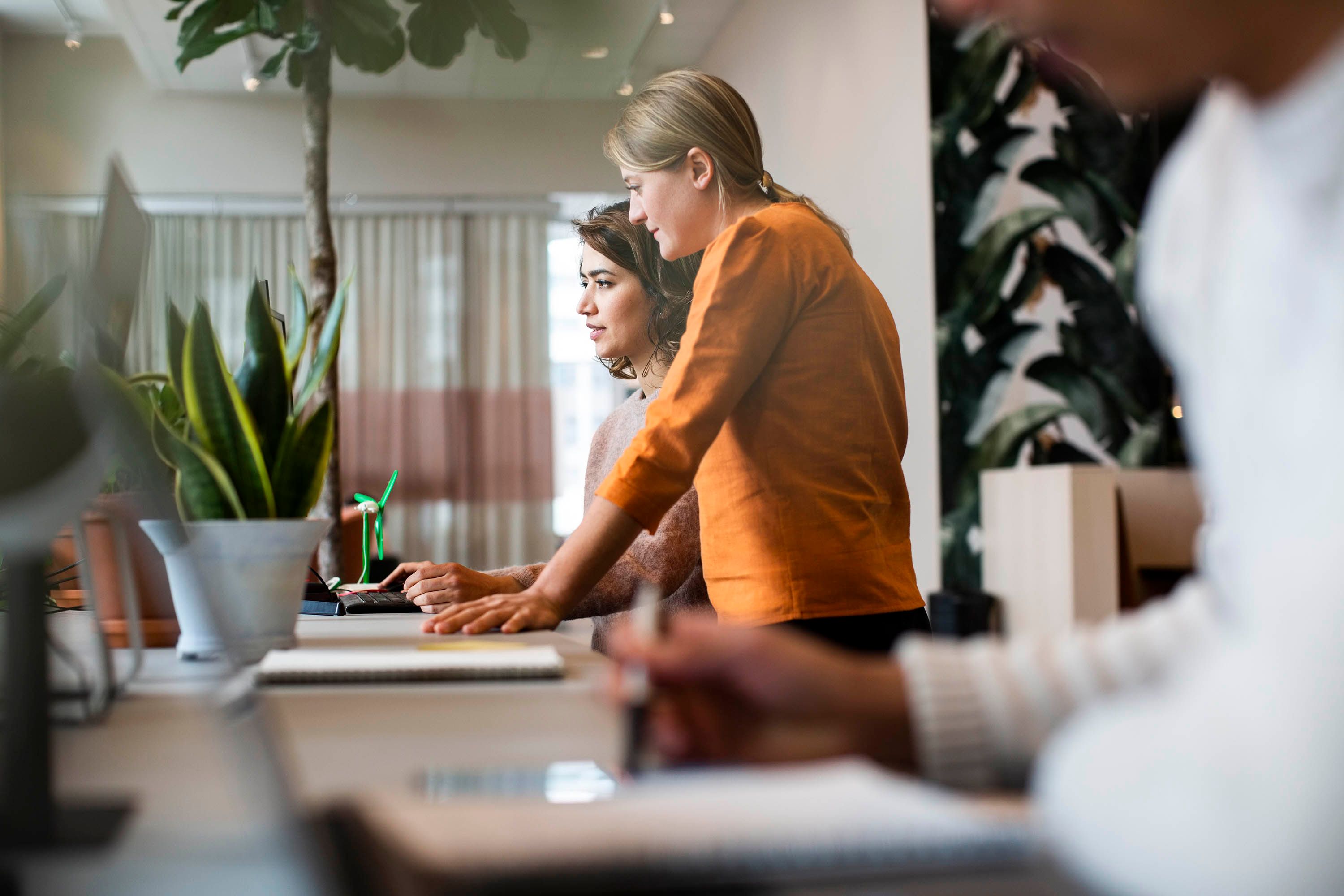Two women standing beside each other at a table while looking at a computer screen