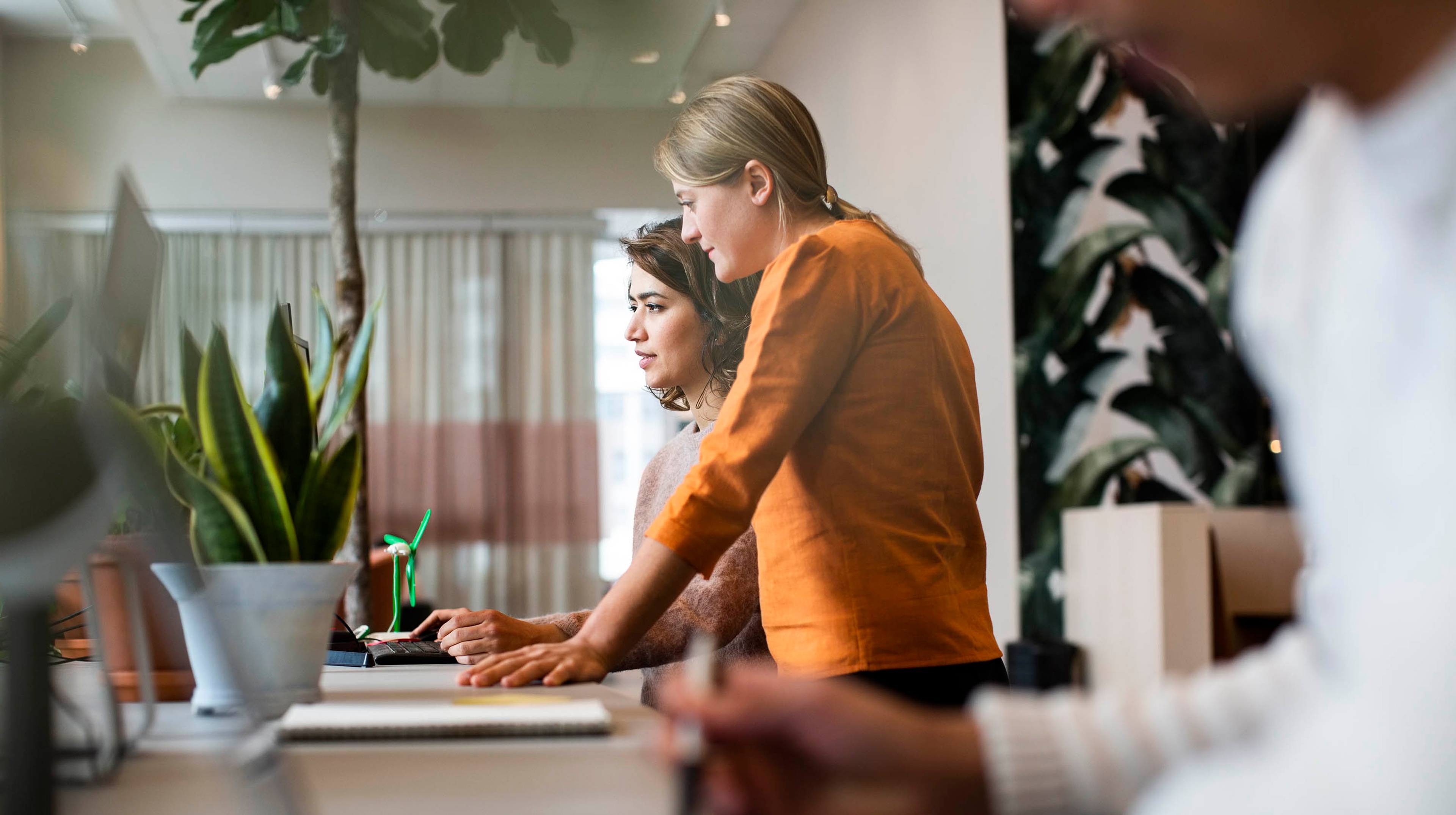 Two women standing beside each other at a table while looking at a computer screen