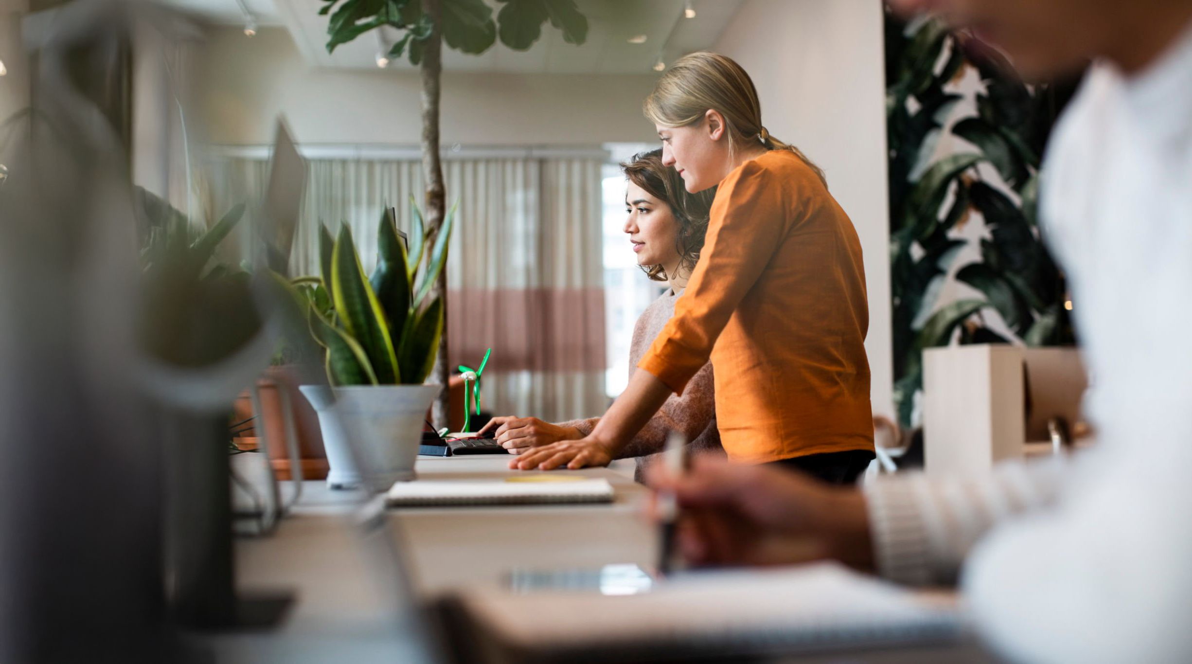 Two women standing beside each other at a table while looking at a computer screen