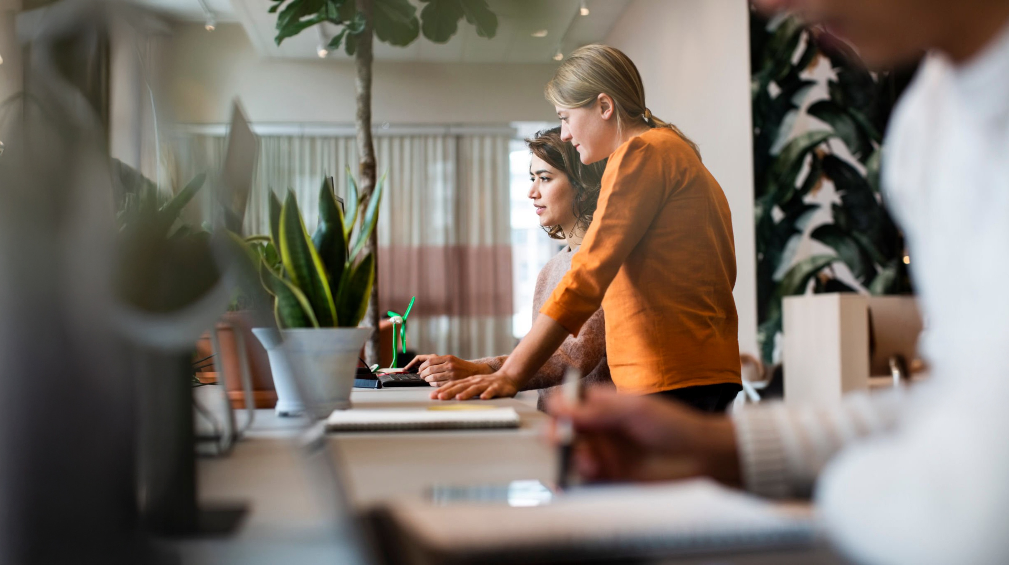 Two women standing beside each other at a table while looking at a computer screen