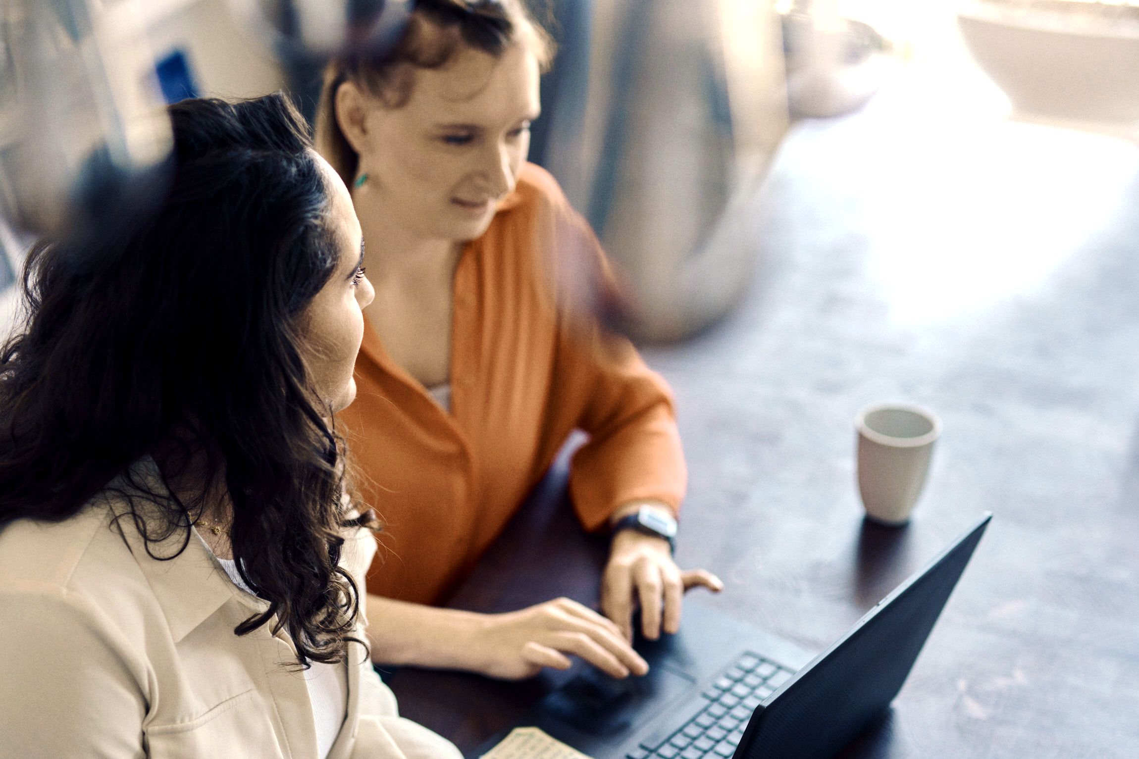 Two women sitting at a table with a laptop and a coffee cup