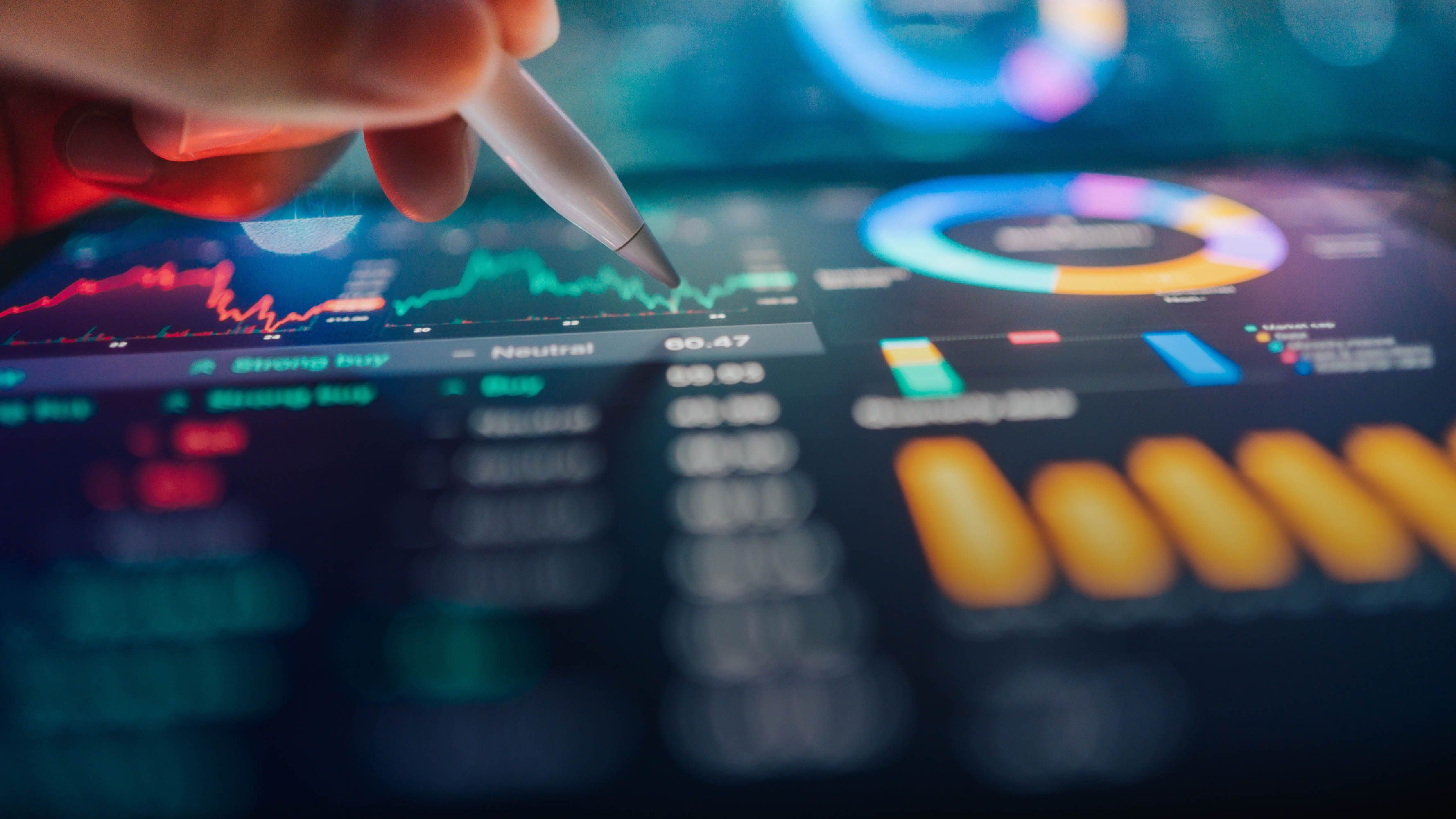 A hand holding a pen above a screen displaying financial data