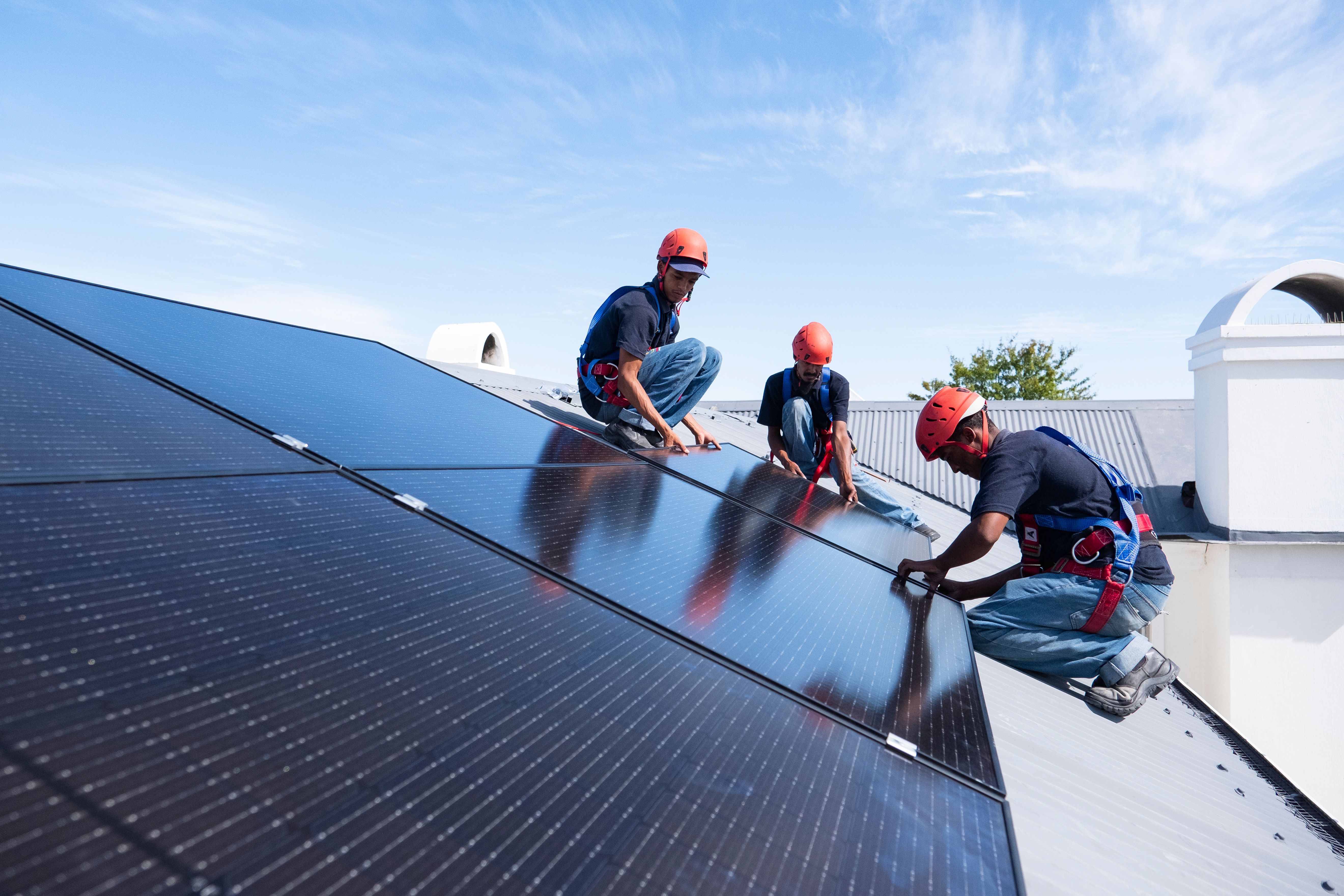 Tre people on a roof installing solar panels