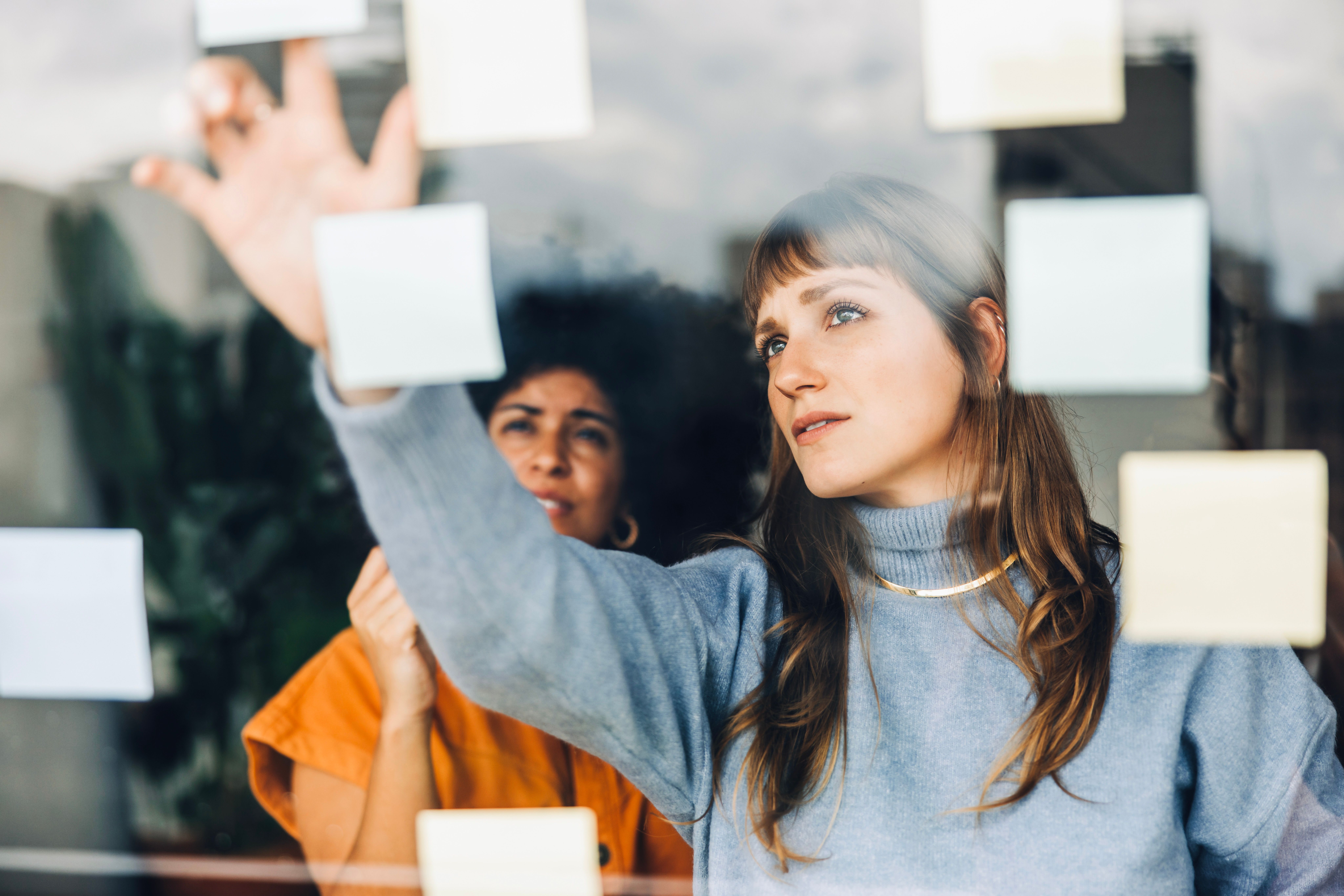 Two women standing infront of a glass wall full of post-it notes