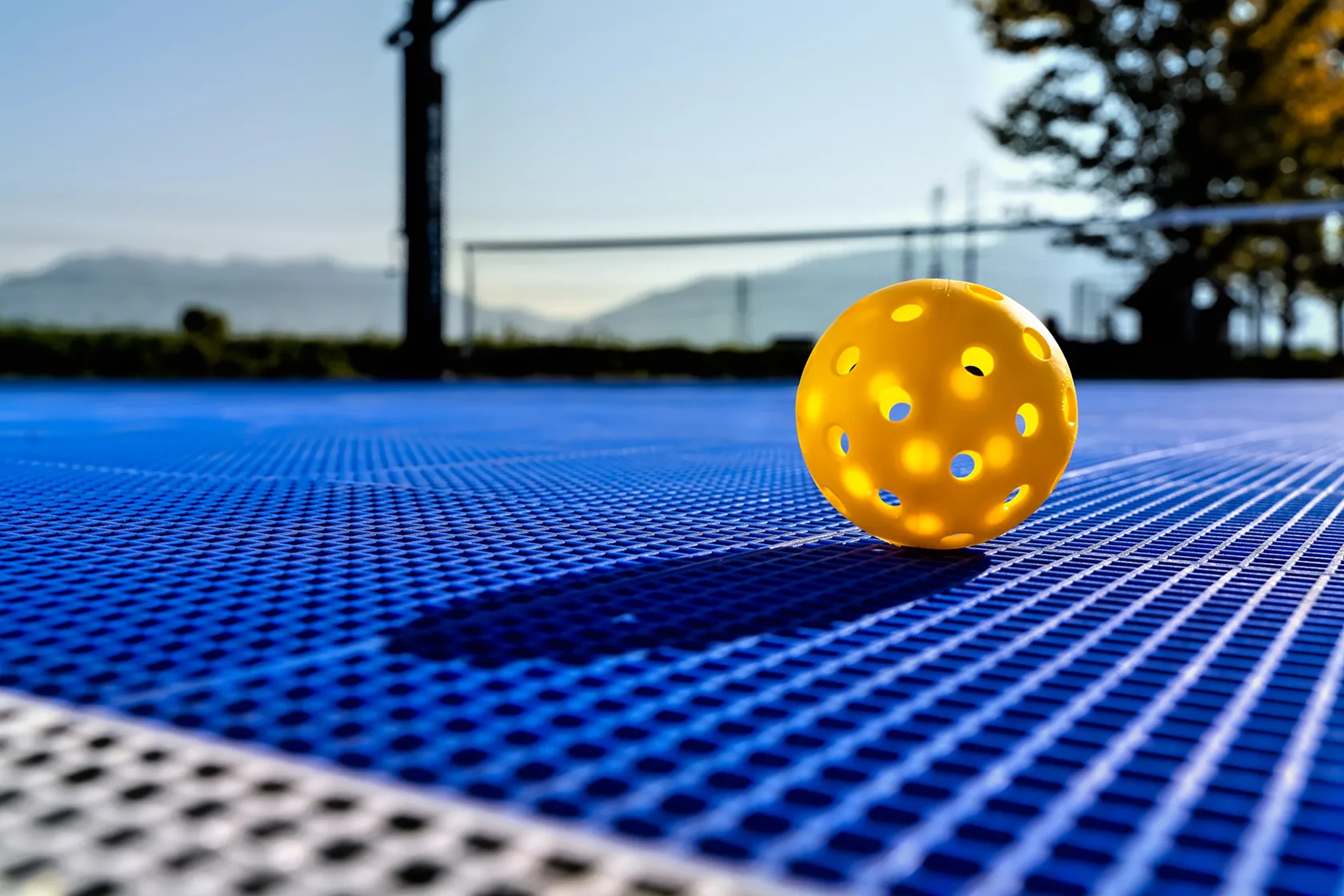 Yellow perforated ball on a blue sports court surface.