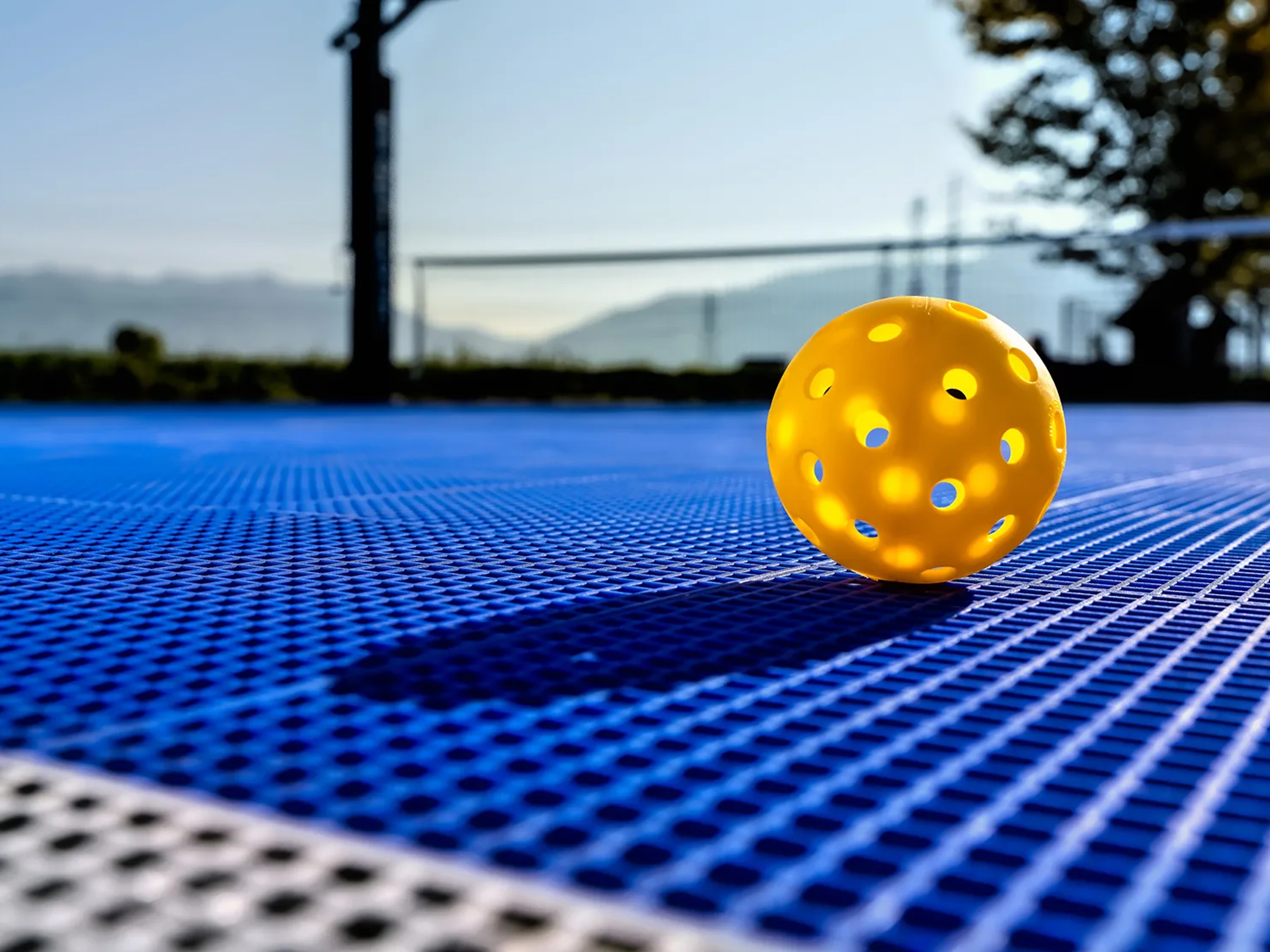 Yellow perforated ball on a blue sports court surface.