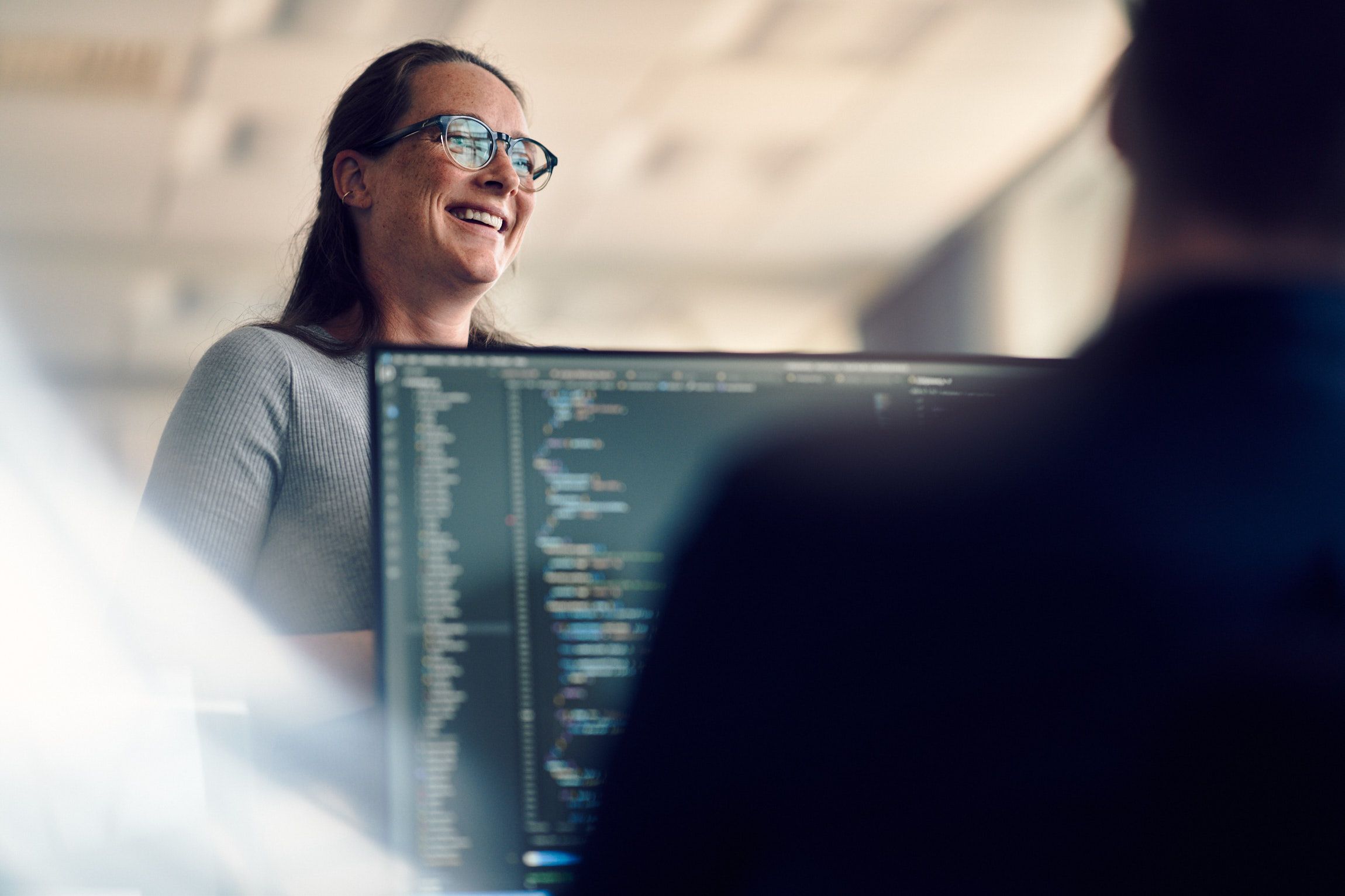Person working on a computer displaying code, and a woman standing behind the computer