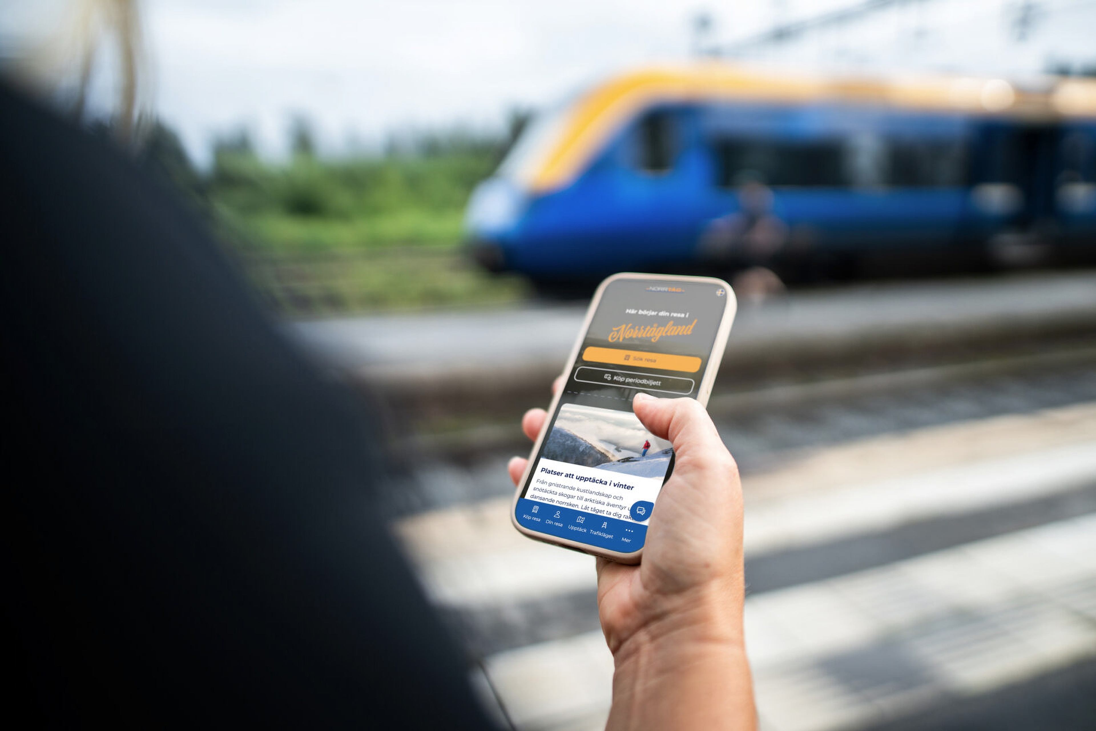 Person holding a smartphone with a transport app at a train platform.