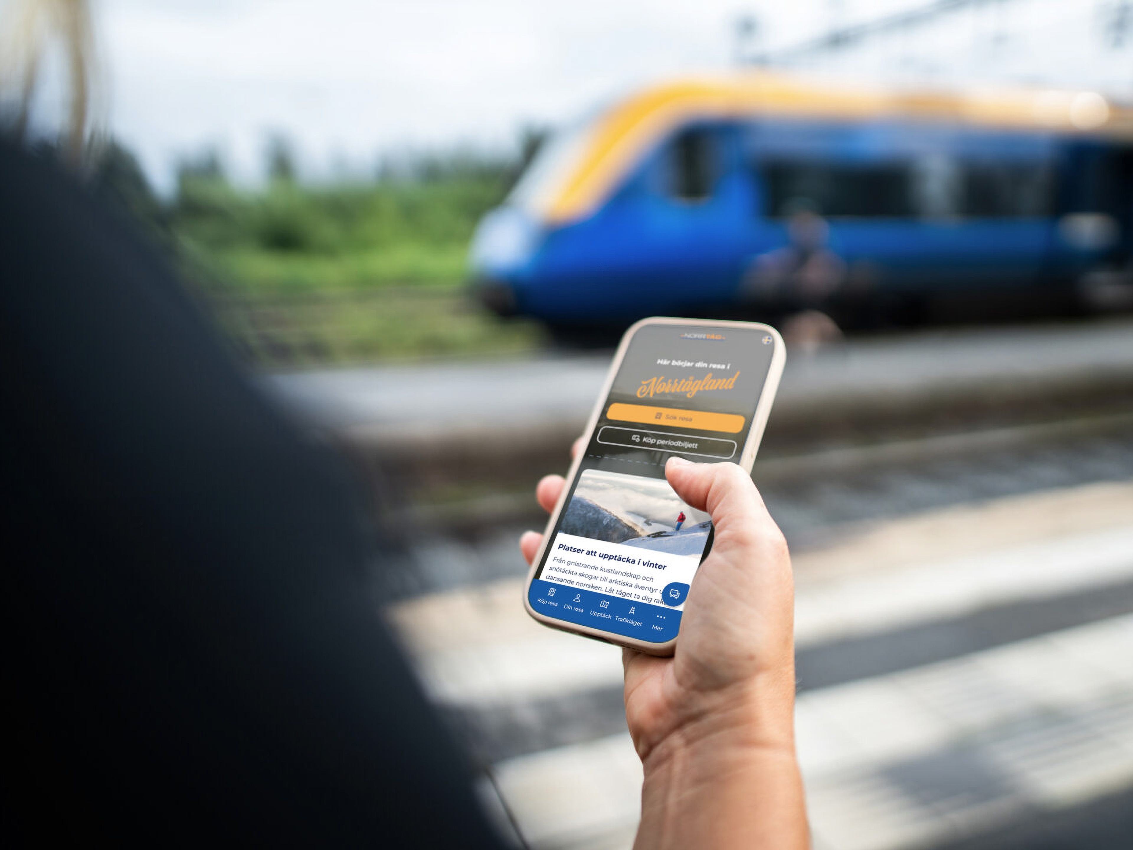 Person holding a smartphone with a transport app at a train platform.