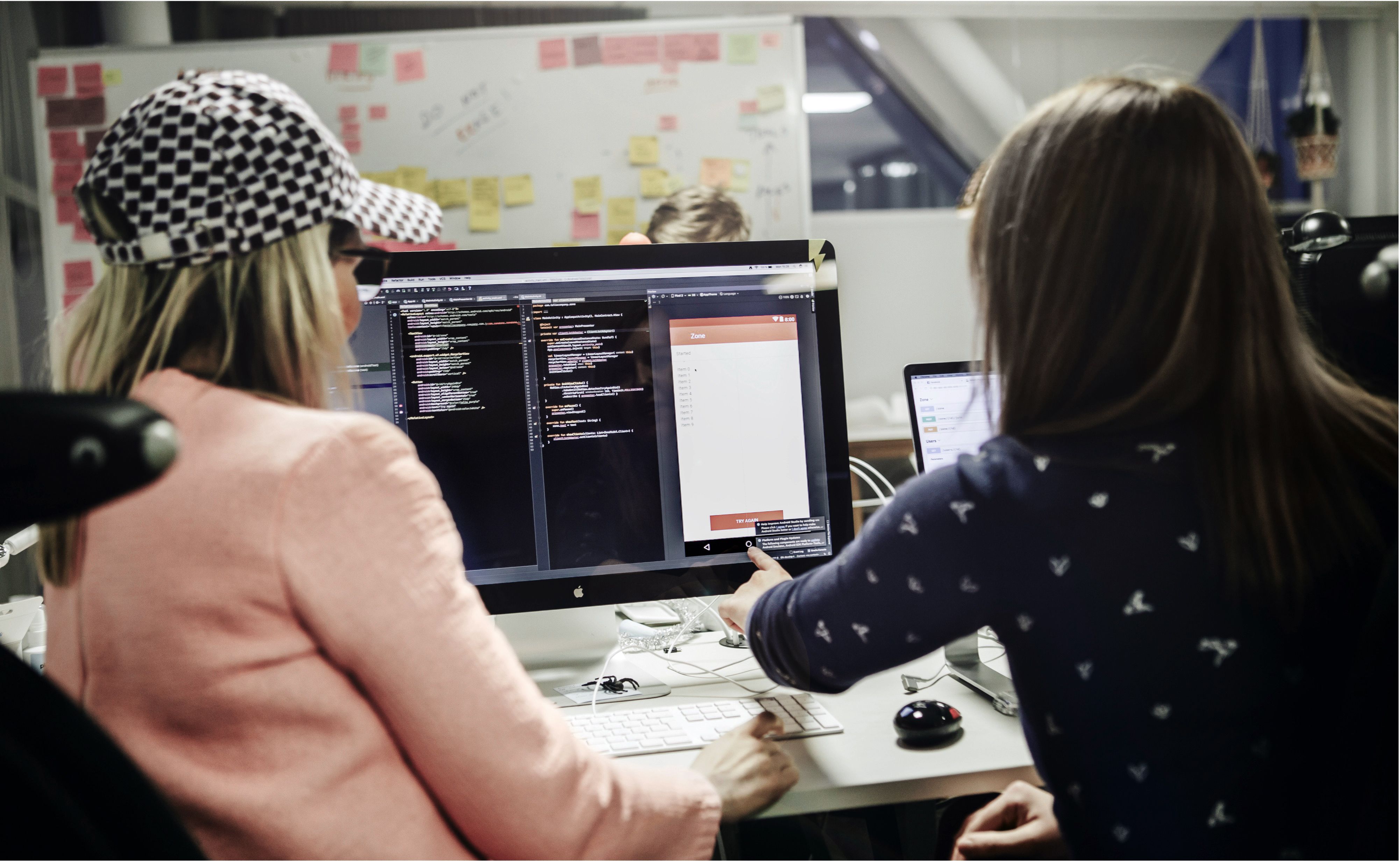 Two women working on a computer displaying code