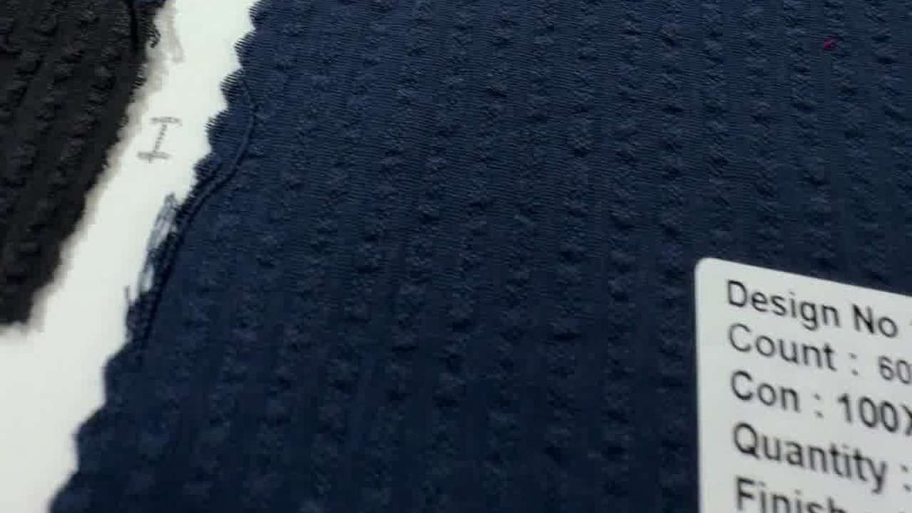 A navy seersucker swatch from a BTCPL swatch book, its puckered stripes catching the light, with a black shade swatch beside it