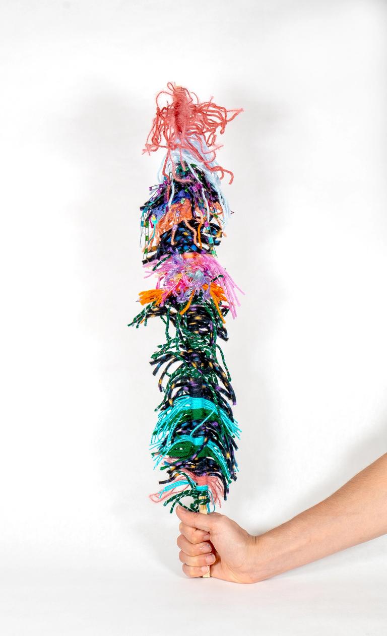 A sculpture resembling a wand, crafted from multi-colored yarn.