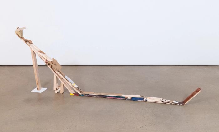 A wood and cardboard structure resembling a Hot Wheels track, with a long flat section followed by a steep, angled ramp upwards.