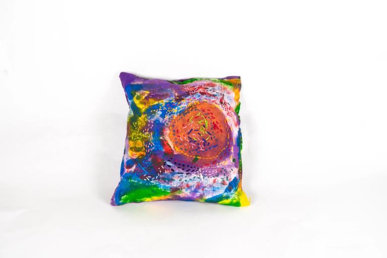 A pillow painted with a vibrant mix of colors, accented with intricate thread-work.