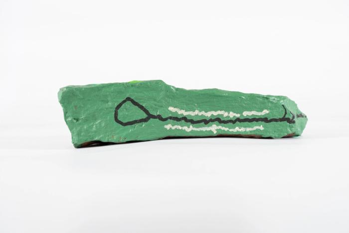 A rock painted green with black and white line work to resemble the head of a dinosaur, alligator or crocodile. 