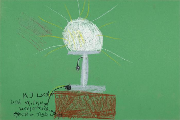 Pastel artwork on green construction paper depicting a hand-drawn lamp on a table. The lamp is gray and white, with yellow lines radiating from it to suggest light.