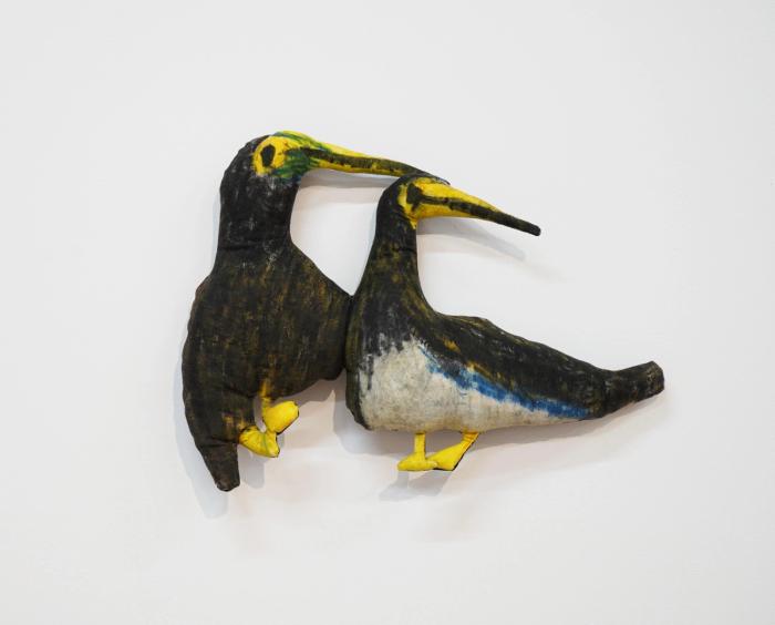 a soft sculpture made of stuffed cotton in the shape of two birds which are painted with black bodies and yellow feet and beaks