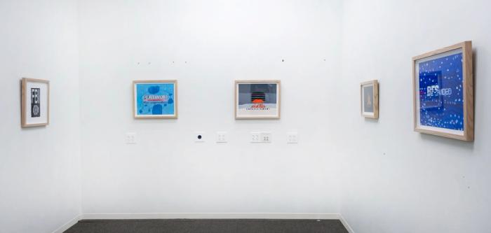 a gallery space with white walls and five artworks in pale wooden frames. the artworks are all different colors and have letters in the center.