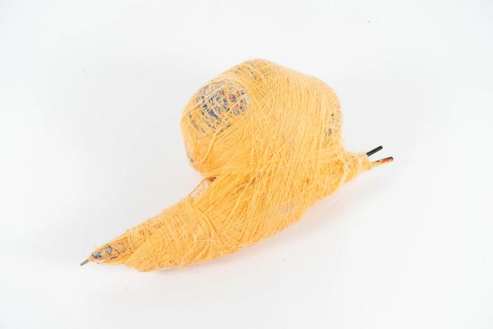 A mixed media, abstract sculpture resembling a snail made of poly thread, paintbrushes, masking tape, saran wrap, foam, and wool yarn.