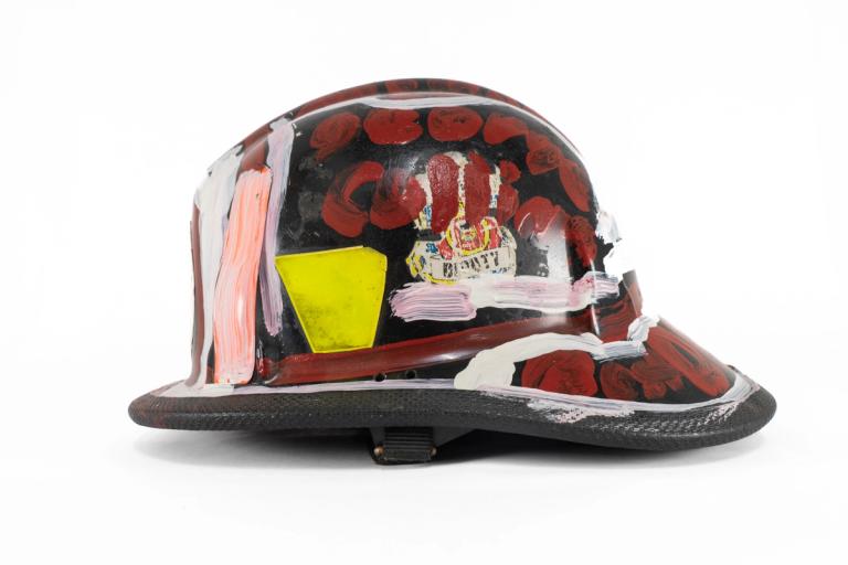 a helmet against a white backdrop. the helmet has a slight brim on the front and larger one on back. insignia of some kind are visible beneath painted marks in red, white, and pink