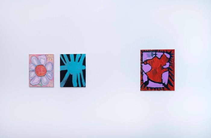 three paintings up close on a white gallery wall. at left, two of the same scale: one is a light pink flower with a big red center, and next is a light blue star-like shape against a dark ground. on the right is a pink and red and black painting with a small dark cross shape and a big amorphous red shape