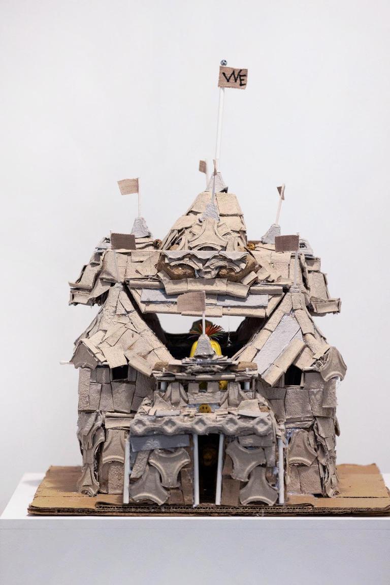 A cardboard sculpture of a castle with flags flying on top. its made of scraps.