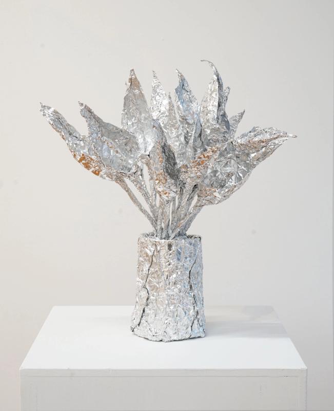 a sculpture of a vase full of lilies made of shiny metal. The flowers are sharp tipped and fill the vase which is set on a white pedestal