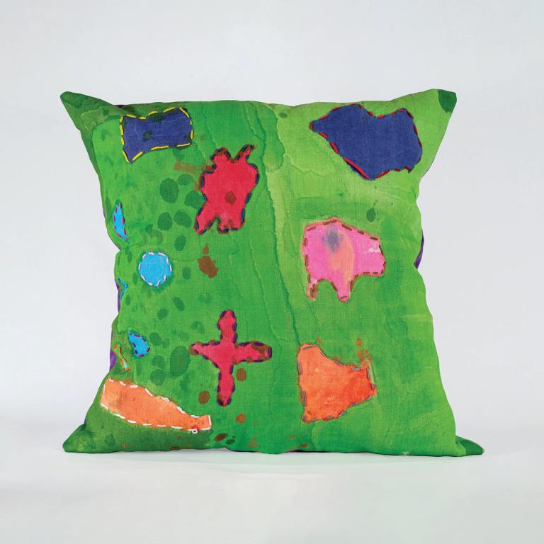 A bright green pillow against a white background. its hand painted with bright red, orange, and purple shapes outlined in embroidery. There are some darker spots that look like the drips of wet paint here and there on the surface
