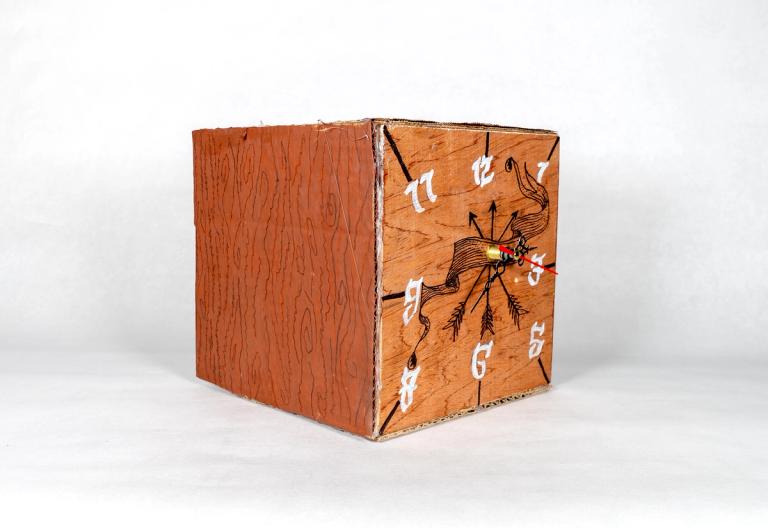 A sculpture of a clock on the side of a redwood-colored cardboard cube, with hand-painted white numbers.