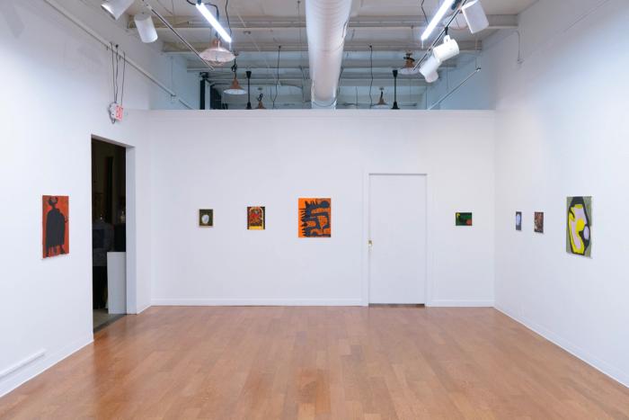 a view of a gallery wall with two walls extending into the foreground on each side. artwork hangs on the walls and there are a closed and open doorway. the floor is wooden