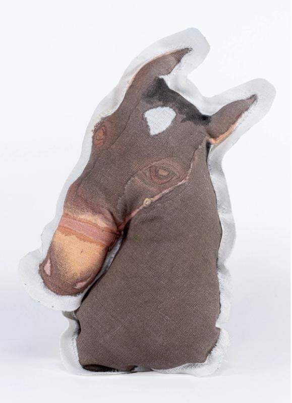a pillow in the shape of a horses head. mostly a dark greyish brown, the nose is light tan and the eyes are distinguishible by slight lightening of color. theres a white spot on the top of the head and some black bangs between the ears