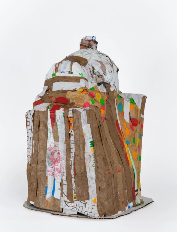 a sculpture loosely in the shape of a building, made of strips of paper, many of which are tan/brown. there are some polka dots in various colors visible, and the top of the building has a small round shape atop a domed 'roof'
