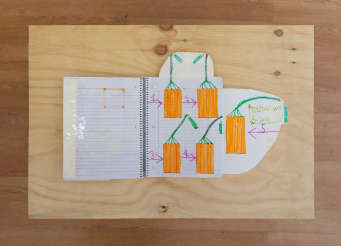 an overhead shot of an open spiral bound notebook. the page we can see has additions taped onto the sides in rounded shapes. the drawing is of five orange rectangles which are connected to green wires.
