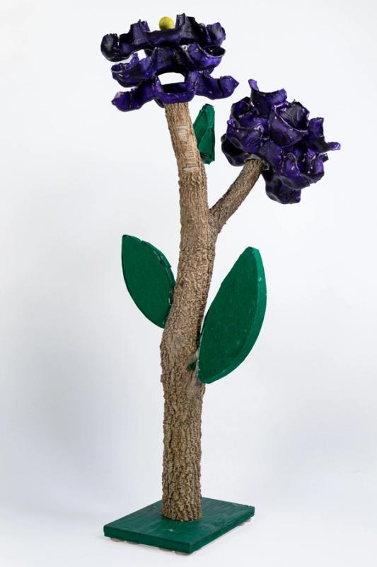 Tree like sculpture with purple flowers and green base photographed against a white background