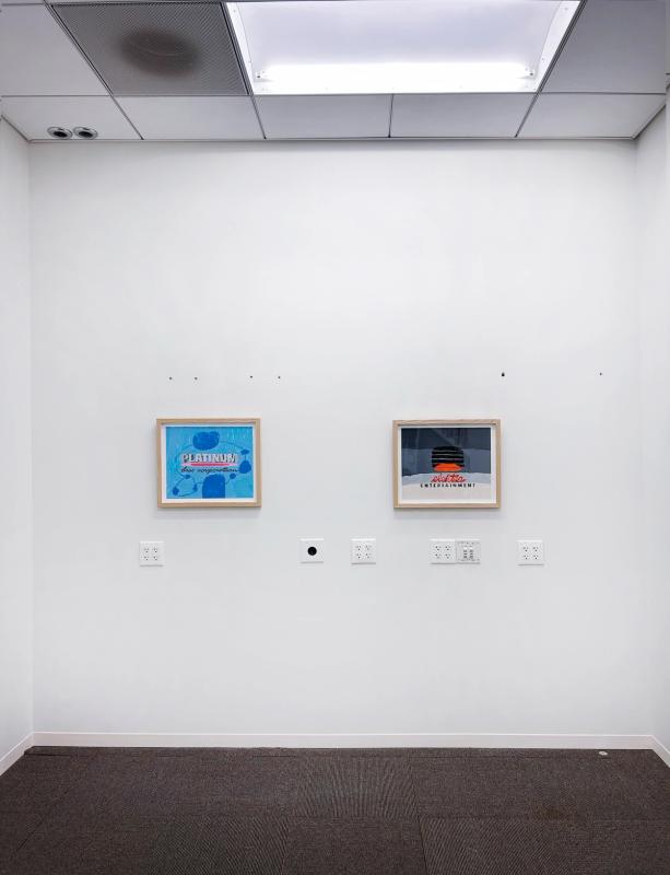 a gallery space with white walls and two artworks in pale wooden frames. both have letters in the center - on left is a light blue painting with darker blue circular forms and on right is a dark grey painting with a light tan section at bottom and a bright orange firm at the center.