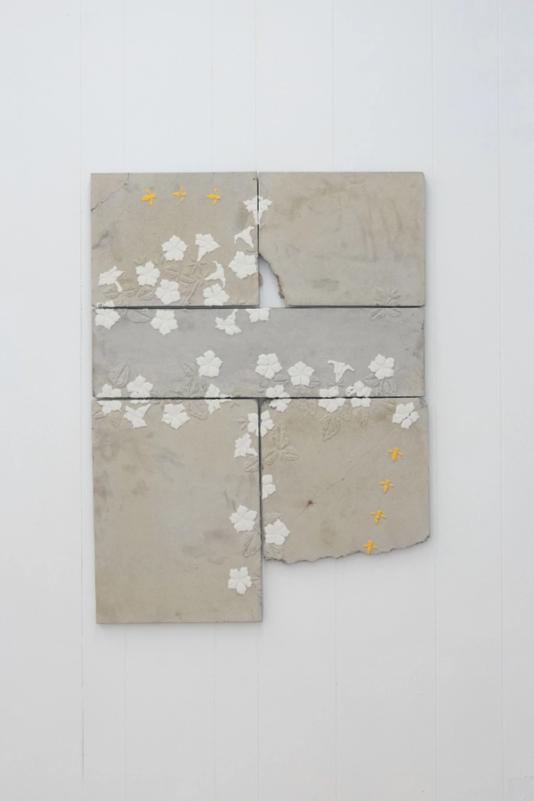 a large work made of cast concrete thats done in 5 sections. there are white flowers strewn across but mostly around the edges where the pieces meet. several yellow wasps fly through. the bottom of the right section is broken with a section missing