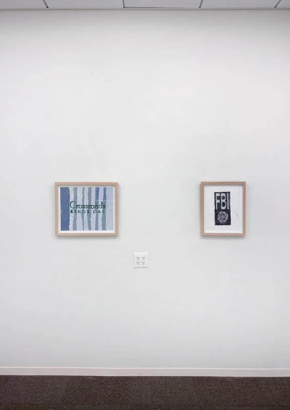 a gallery space with white walls and two artworks in pale wooden frames. both have letters in the center - on left: dark and light grey stripes run vertically and there is green text in the middle that says 'crossroads kings oak' on right: a white boarder with a dark rectangle in the middle that says 'FBI'  