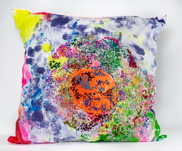 A custom embroidered pillow with a vibrant mix of colors including pink, blue, green, and orange, featuring a geometric pattern.