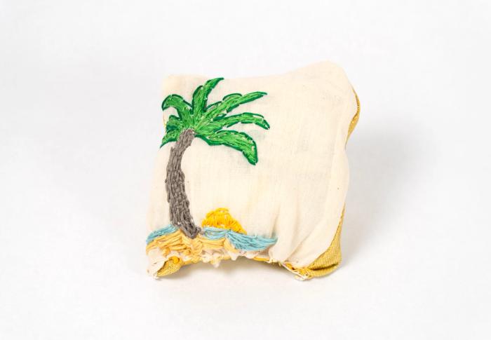 Fabric art piece featuring a woven palm tree on a sandy beach.