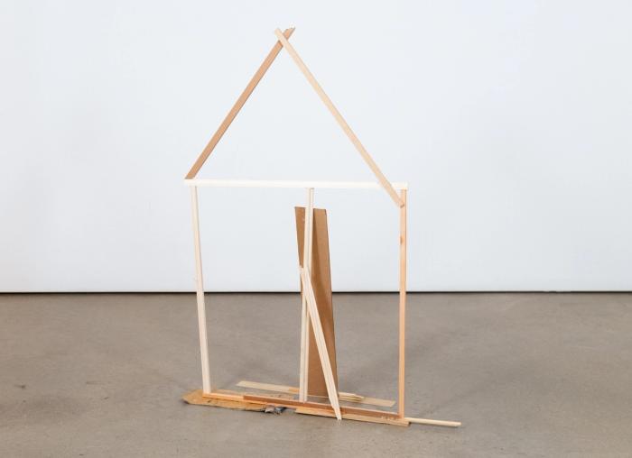 A bare wood and cardboard sculpture resembling an A-frame house structure.