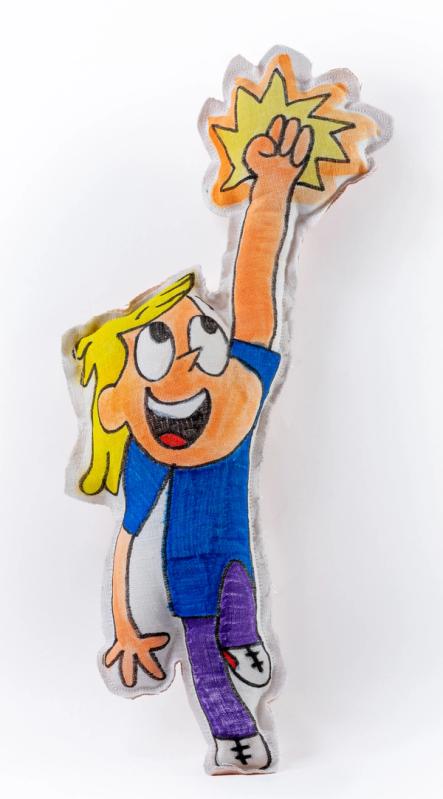 a pillow shaped like a cartoon figure with arm upstretched in a fist and a star of energy surrounding the fist. the figure has orangey pink skin and exaggerated features and is wearing purple pants and blue shirt.