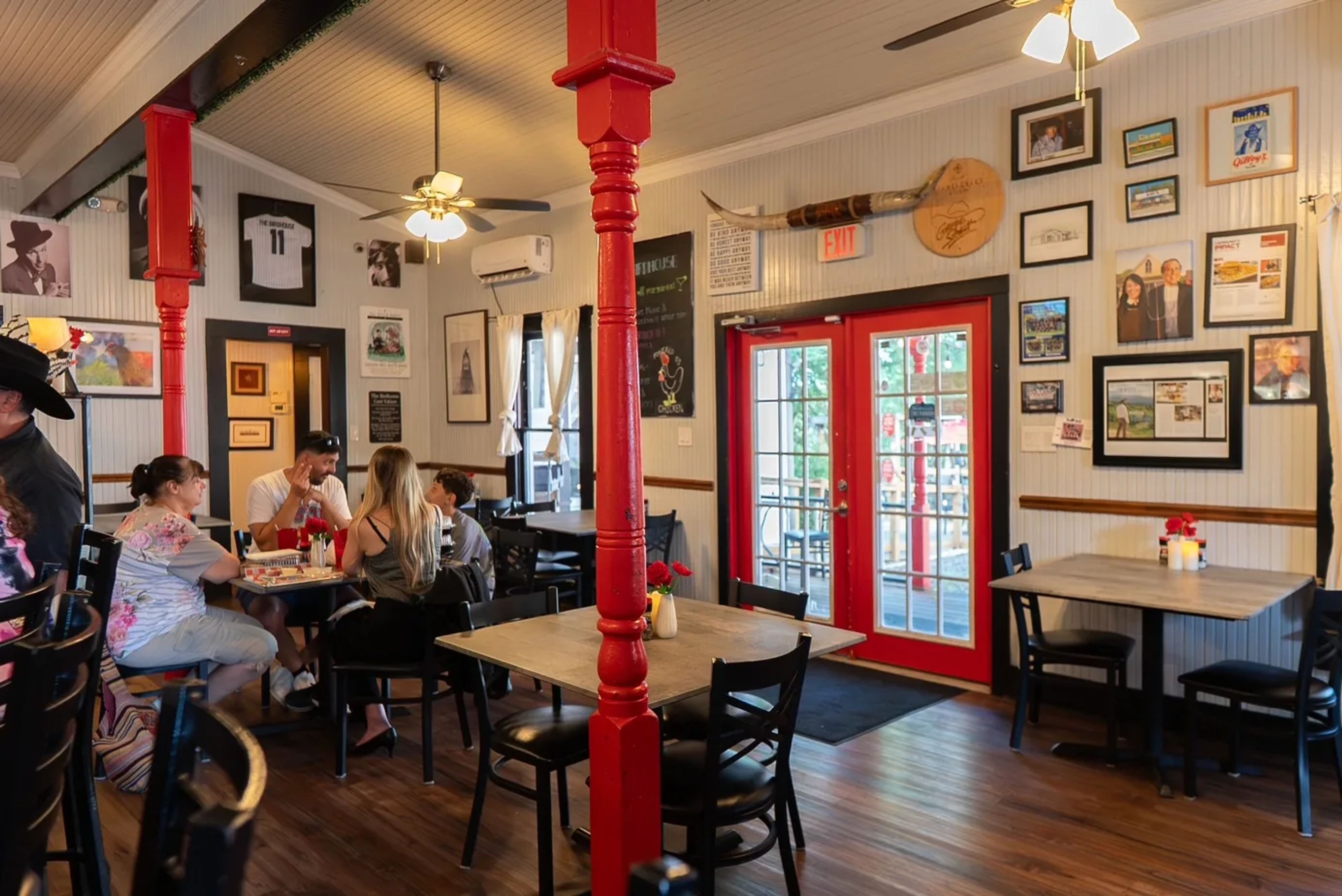 The Birdhouse dining room, with red posts, black chairs, guests at a table, framed photos on white walls and red glass doors