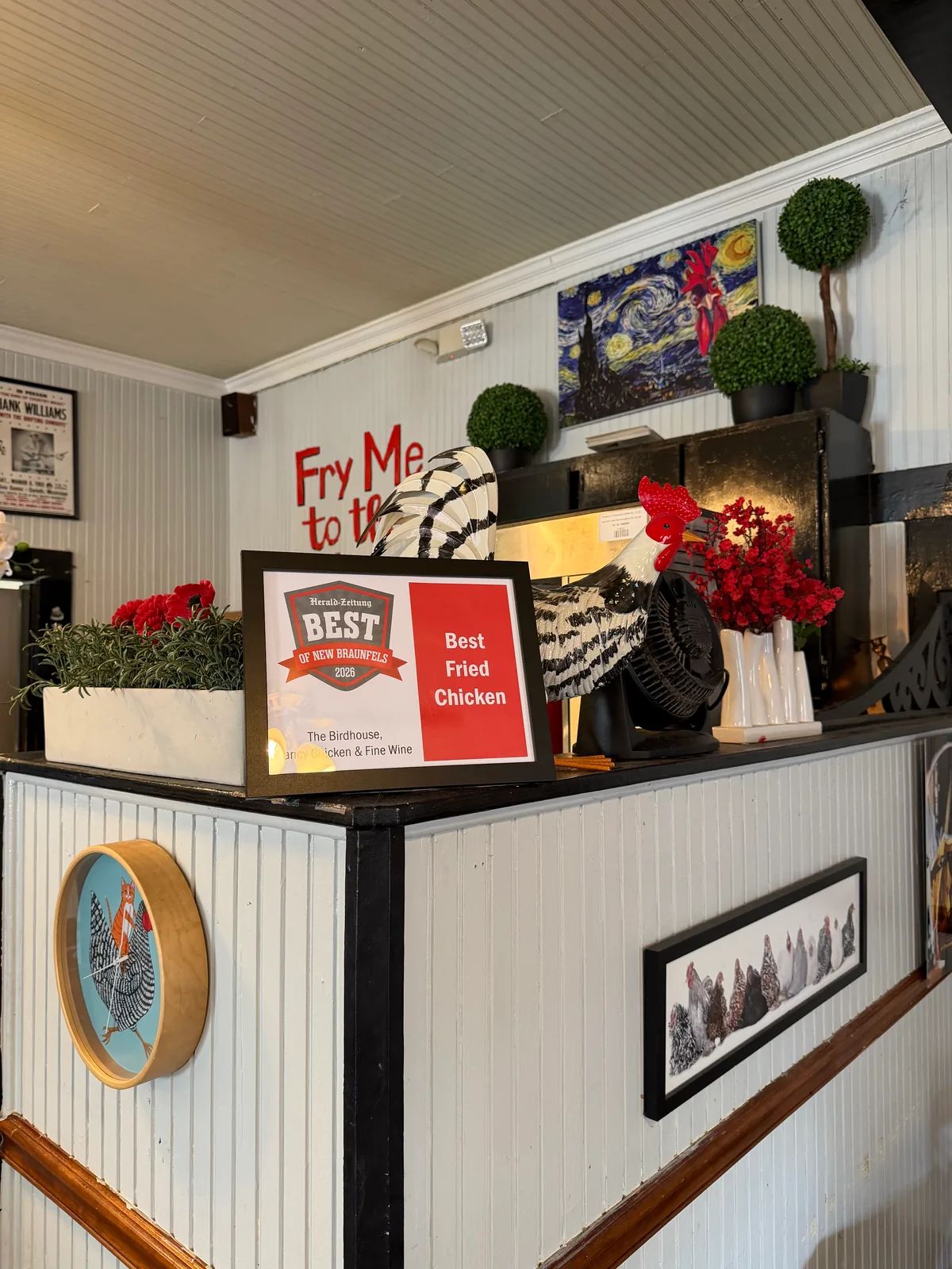 The Herald-Zeitung Best of New Braunfels 2026 Best Fried Chicken certificate on the counter, beside a black and white ceramic rooster and red flowers