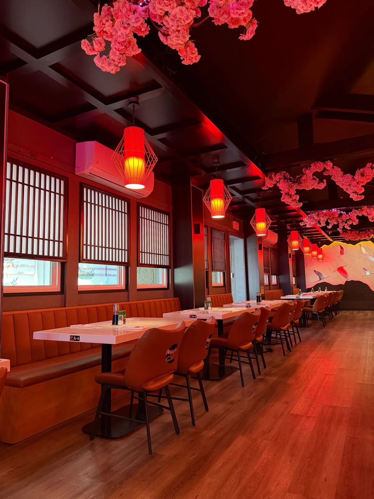 The empty dining room: red lanterns and pink blossom garlands over a long booth, lattice windows and a bird mural at the far end
