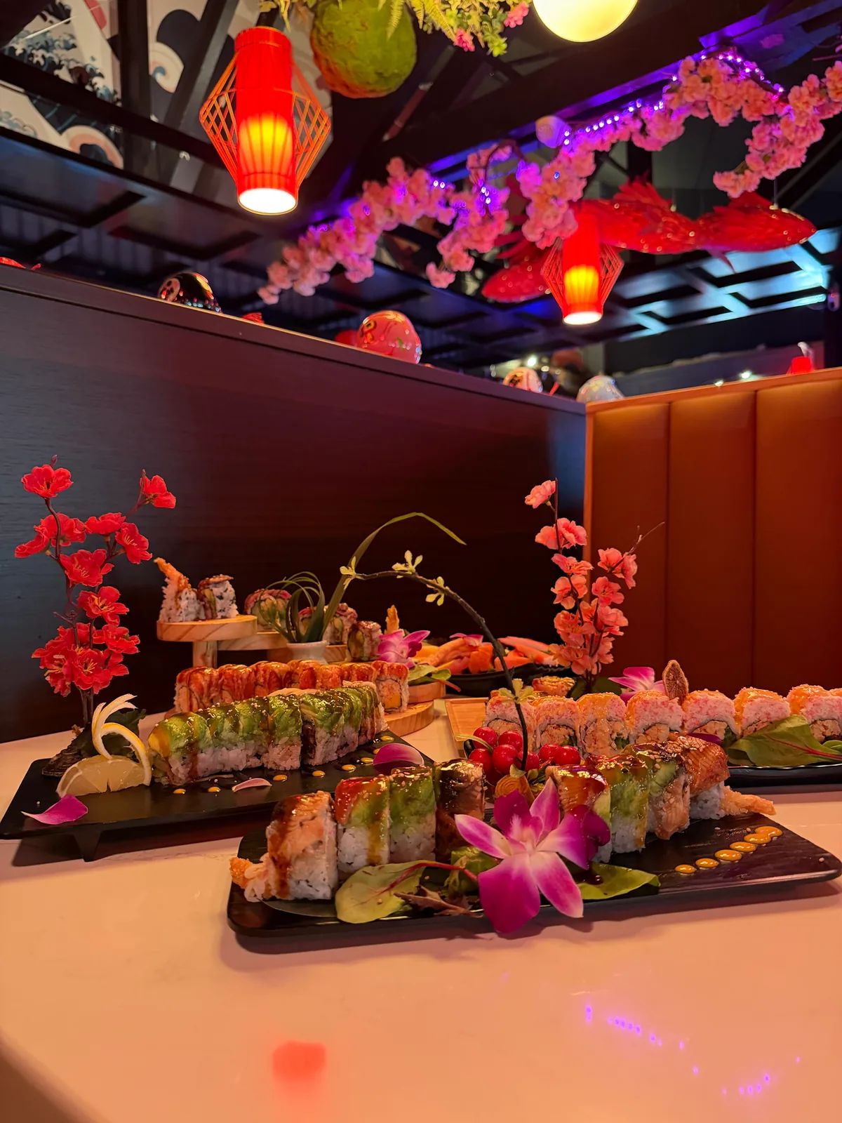 Sushi rolls on black trays, garnished with orchids and blossom branches, under red lanterns